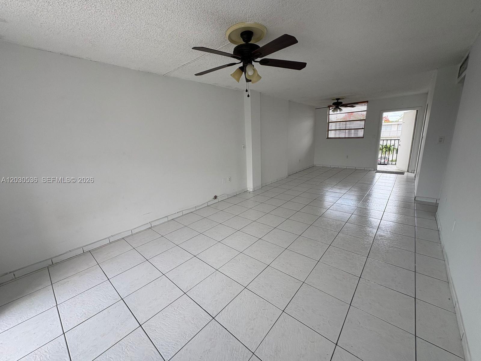 An empty room features white tiled floors, white walls, and two ceiling fans — 14185 SW 87th St # 304, Miami FL 33183, MIAMI, FL