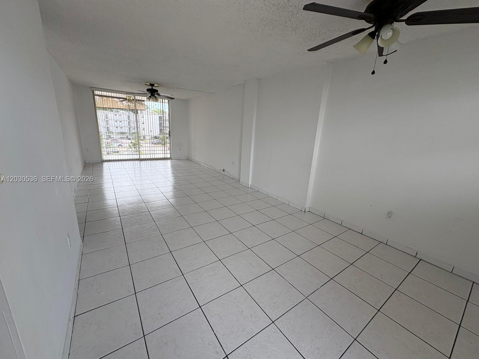 An empty room features white tiled floors, white walls, and two ceiling fans — 14185 SW 87th St # 304, Miami FL 33183, MIAMI, FL