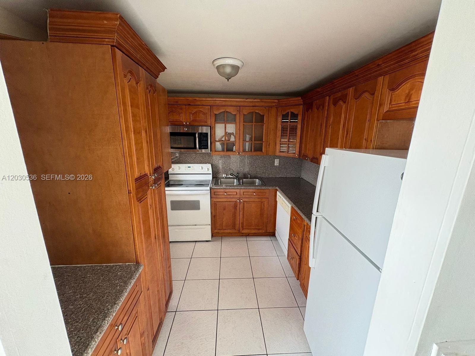 A kitchen features wood cabinets, white appliances, tile flooring, and a granite-style countertop — 14185 SW 87th St # 304, Miami FL 33183, MIAMI, FL
