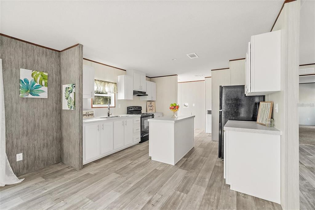 A kitchen features white cabinets, a central island, and wood-look flooring in an open space — 1259 ROSEWOOD STREET, BUNNELL, FL