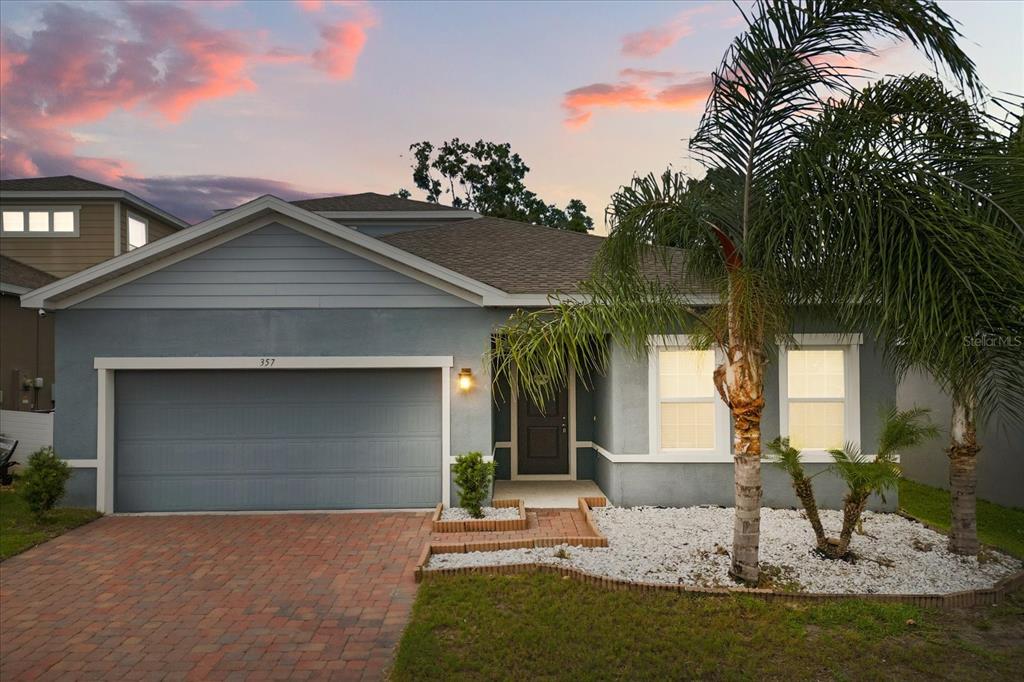 A single-story house with a gray stucco exterior, a brick driveway, and a palm tree — 357 SIESTA VISTA COURT, DAVENPORT, FL