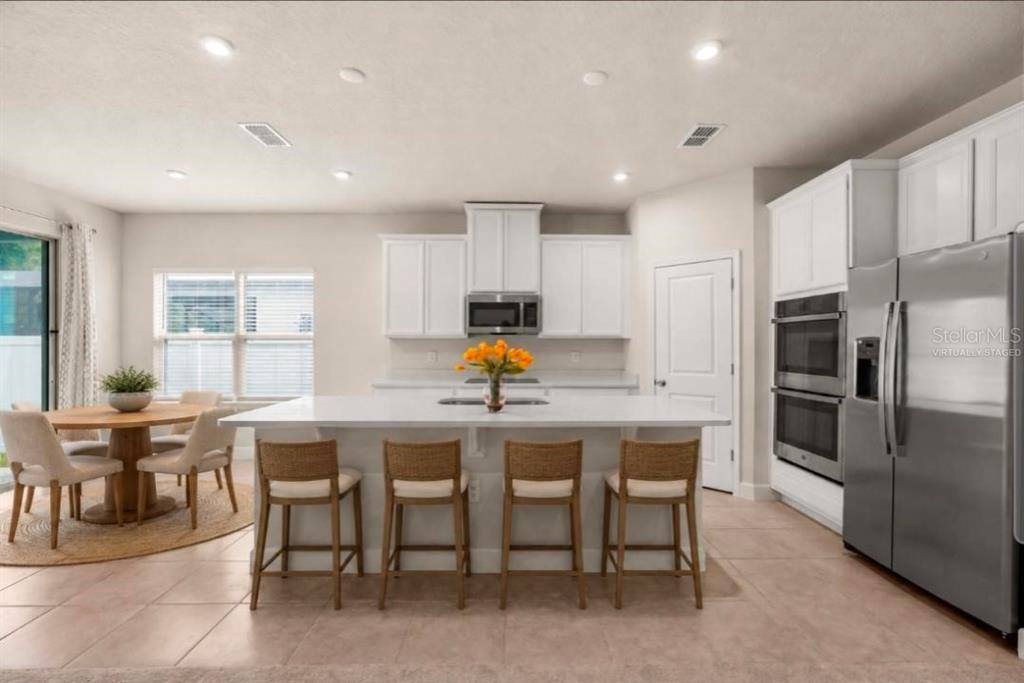 A kitchen features white cabinets, a large island with four stools, and stainless steel appliances — 357 SIESTA VISTA COURT, DAVENPORT, FL