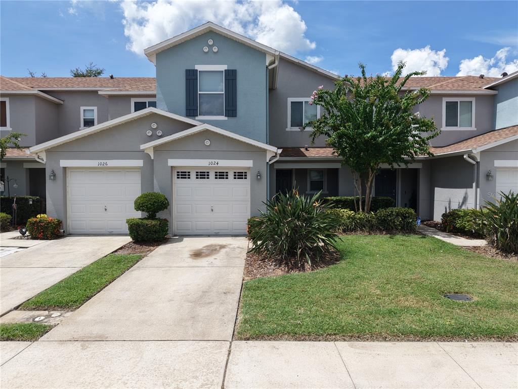 A two-story townhouse exterior features gray siding, a blue accent wall, and two garage doors — 1024 CHALCEDONY STREET, KISSIMMEE, FL