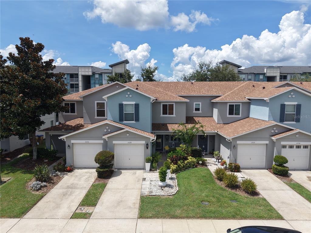 An exterior view of a multi-unit townhouse complex with attached garages and a shared lawn — 1024 CHALCEDONY STREET, KISSIMMEE, FL