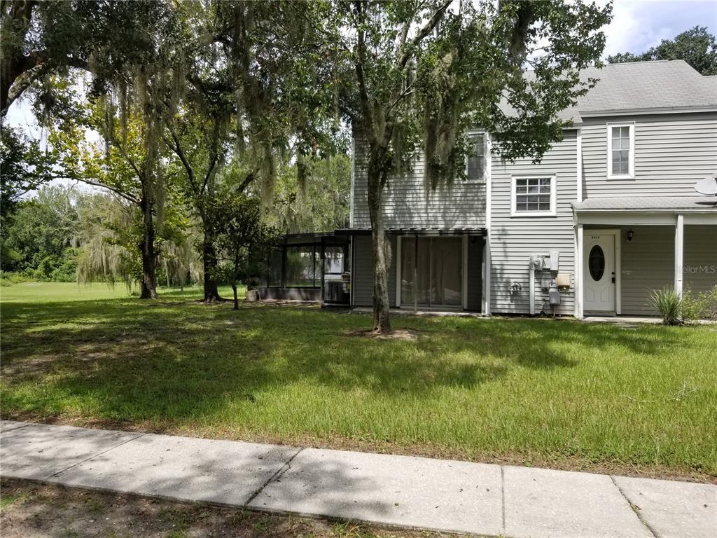 A two-story gray-sided townhouse features a screened-in patio and a grassy yard with trees — 8202 BROWARD PLACE, TEMPLE TERRACE, FL