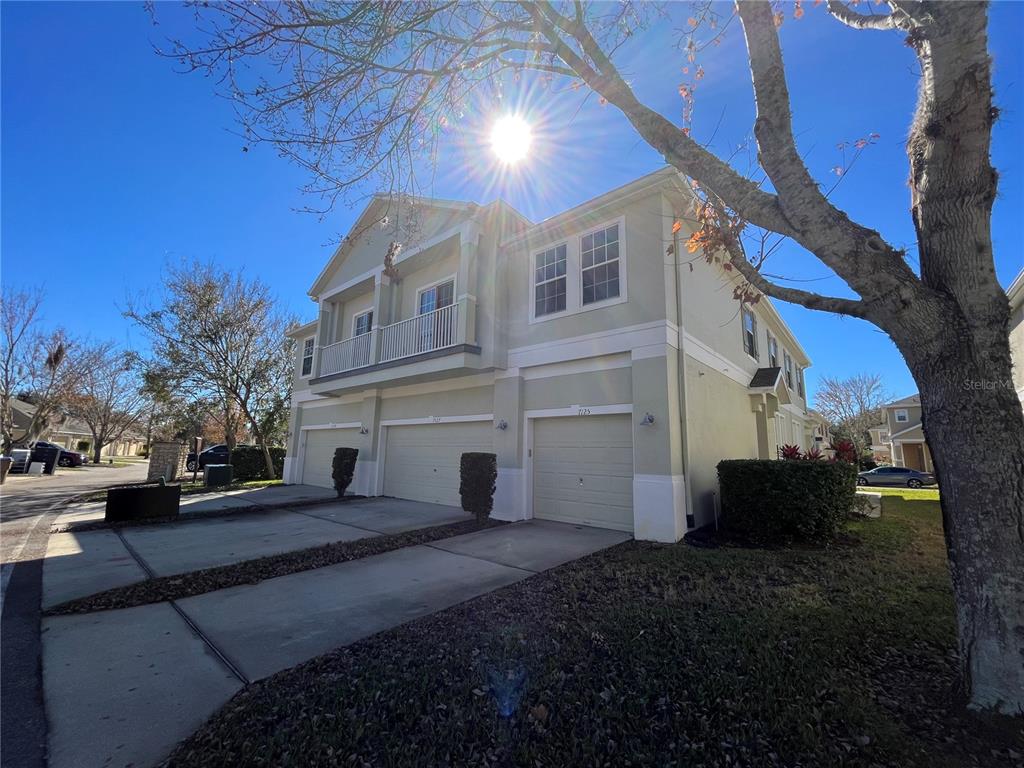 A two-story townhouse exterior features a light-colored facade, three garage doors, and a balcony — 7125 RED LANTERN DR UNIT 17A, ST CLOUD, FL