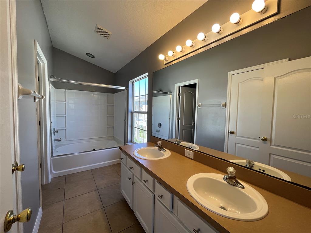 A bathroom features a double vanity with a tan countertop, a large mirror, and a tub-shower — 7125 RED LANTERN DR UNIT 17A, ST CLOUD, FL