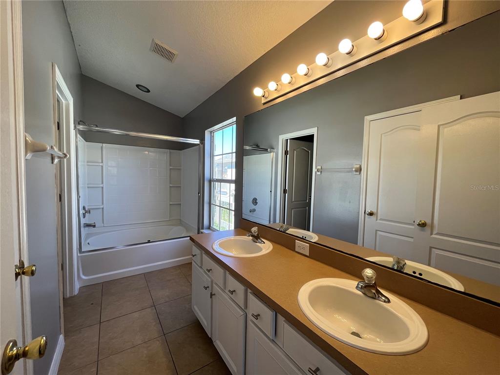 A bathroom features a double vanity with a tan countertop, a large mirror, and a tub-shower — 7125 RED LANTERN DR UNIT 17A, ST CLOUD, FL
