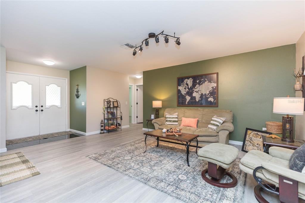 A living room features light wood-look flooring, a green accent wall, and a world map — 8423 PEBBLE DRIVE, PORT RICHEY, FL