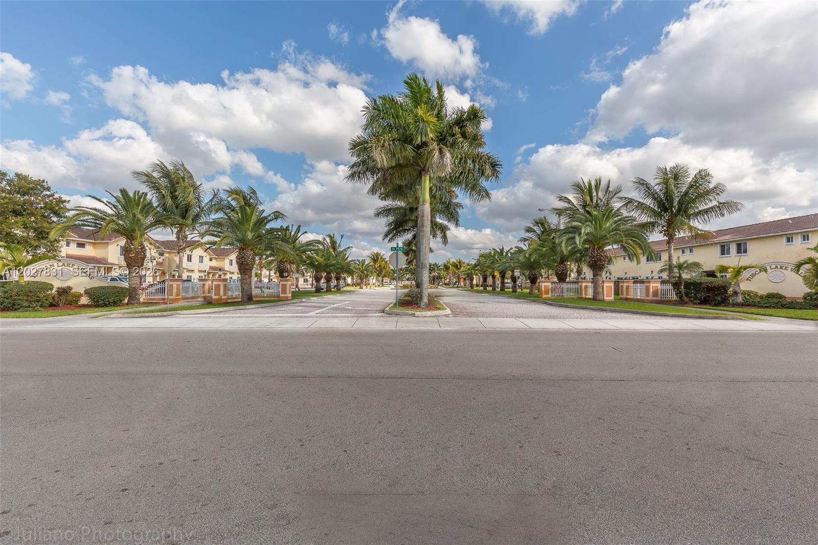 A paved street leads into a residential community lined with palm trees and townhouses — 7488 NW 181st St # 7488, Hialeah FL 33015, HIALEAH, FL