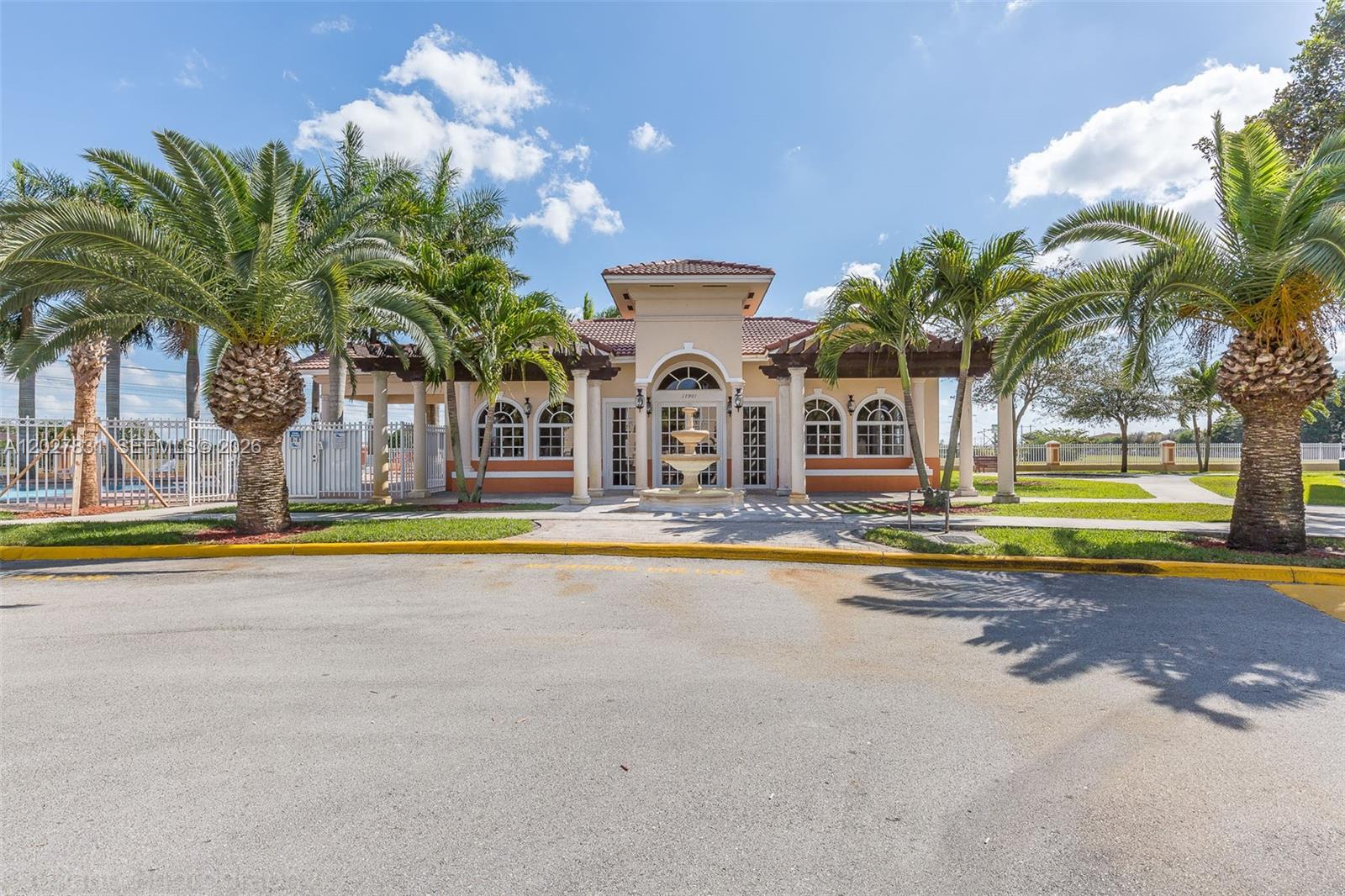 A tan clubhouse with a central fountain, arched windows, and palm trees in front — 7488 NW 181st St # 7488, Hialeah FL 33015, HIALEAH, FL