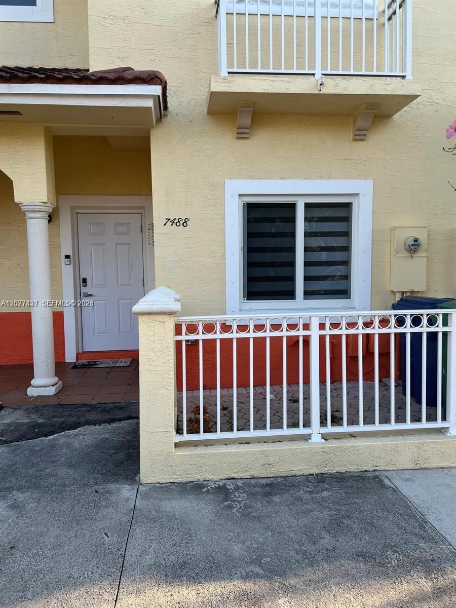 The exterior of a two-story residential building features a white door and a fenced patio — 7488 NW 181st St # 7488, Hialeah FL 33015, HIALEAH, FL