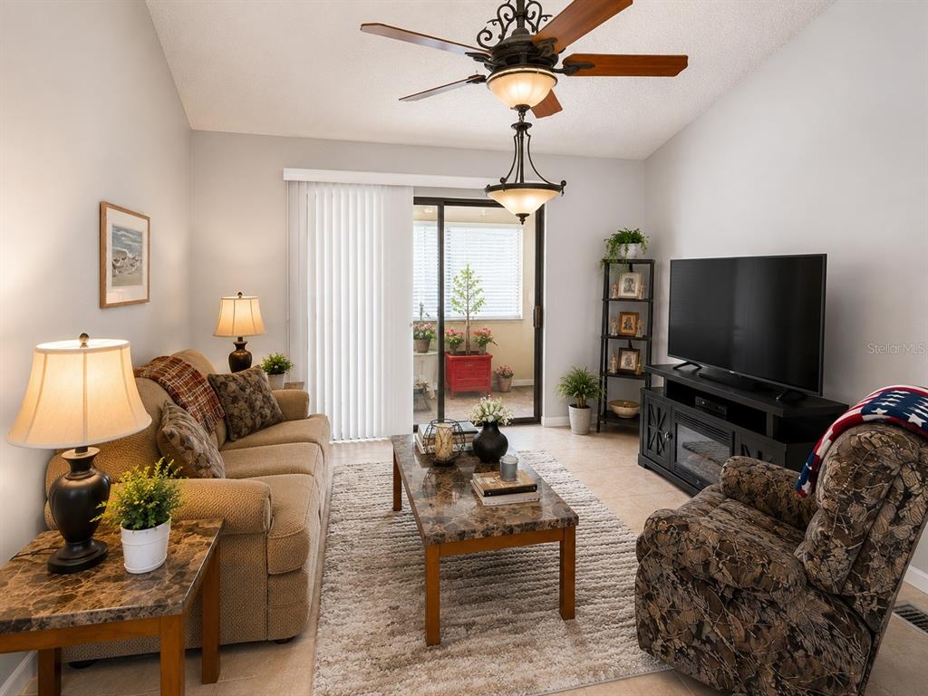 A living room features a beige sofa, patterned armchair, coffee table, and a sliding glass door — 1126 FAIRVILLA DRIVE UNIT 1126, NEW SMYRNA BEACH, FL