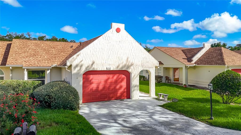 A single-story house features a red garage door, textured white walls, and a brown roof — 11543 ORLEANS LANE, PORT RICHEY, FL