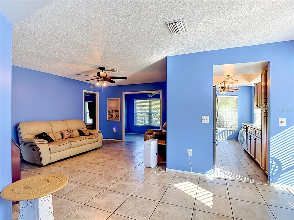A living room with blue walls, tile flooring, and a beige sofa leads to a kitchen — 11543 ORLEANS LANE, PORT RICHEY, FL