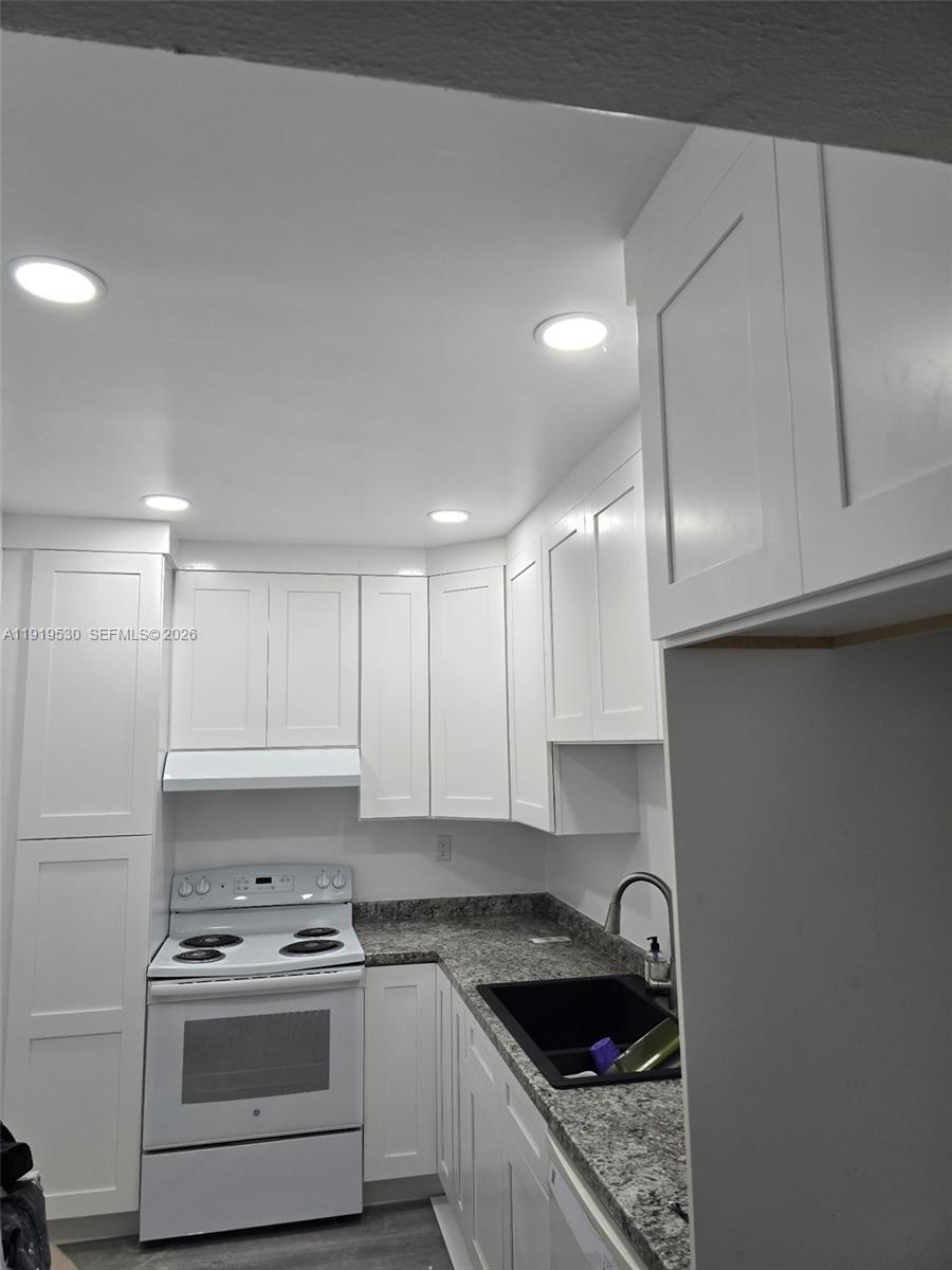 This kitchen features white cabinets, granite countertops, a black sink, and a white stove — 9159 SW 77th Ave # 211, Miami FL 33156, MIAMI, FL