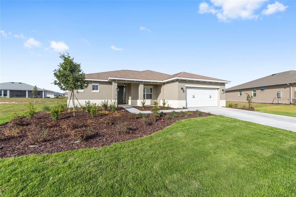 A single-story house with a beige stucco exterior, a two-car garage, and a landscaped yard — 10657 SW 102ND LANE, OCALA, FL