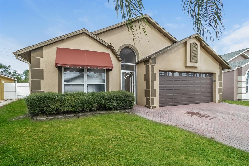 A tan single-story house with a red awning, arched window, and a brick driveway — 120 LAKEBREEZE CIRCLE, LAKE MARY, FL