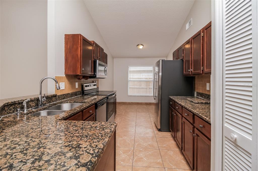 A galley kitchen features dark wood cabinets, granite countertops, stainless steel appliances, and tile flooring — 120 LAKEBREEZE CIRCLE, LAKE MARY, FL