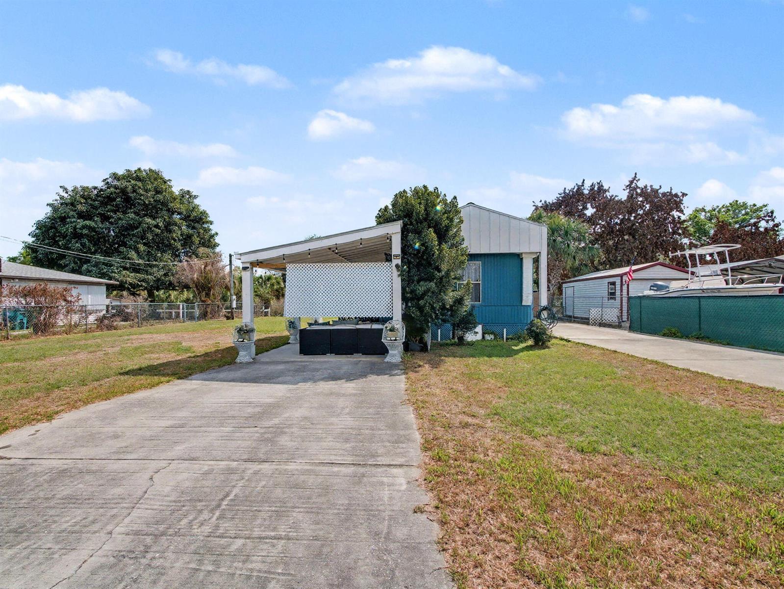 A blue mobile home features a concrete driveway and a covered patio with lattice screening — 4024 SE 29th Court, Okeechobee FL 34974, OKEECHOBEE, FL
