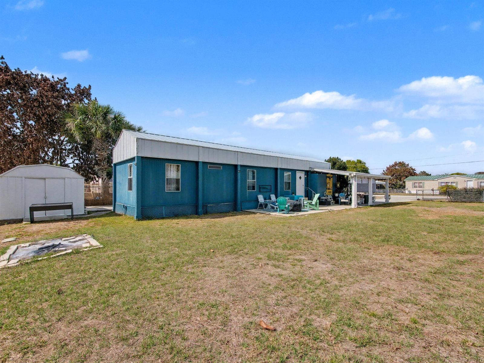A blue mobile home with a metal roof and a patio sits on a grassy lot — 4024 SE 29th Court, Okeechobee FL 34974, OKEECHOBEE, FL