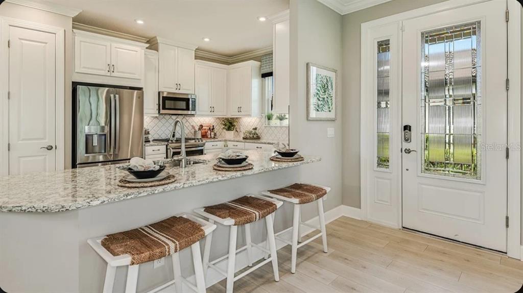 A kitchen with white cabinets, granite countertops, and a breakfast bar with three stools — 14513 DERNA TERRACE, BRADENTON, FL