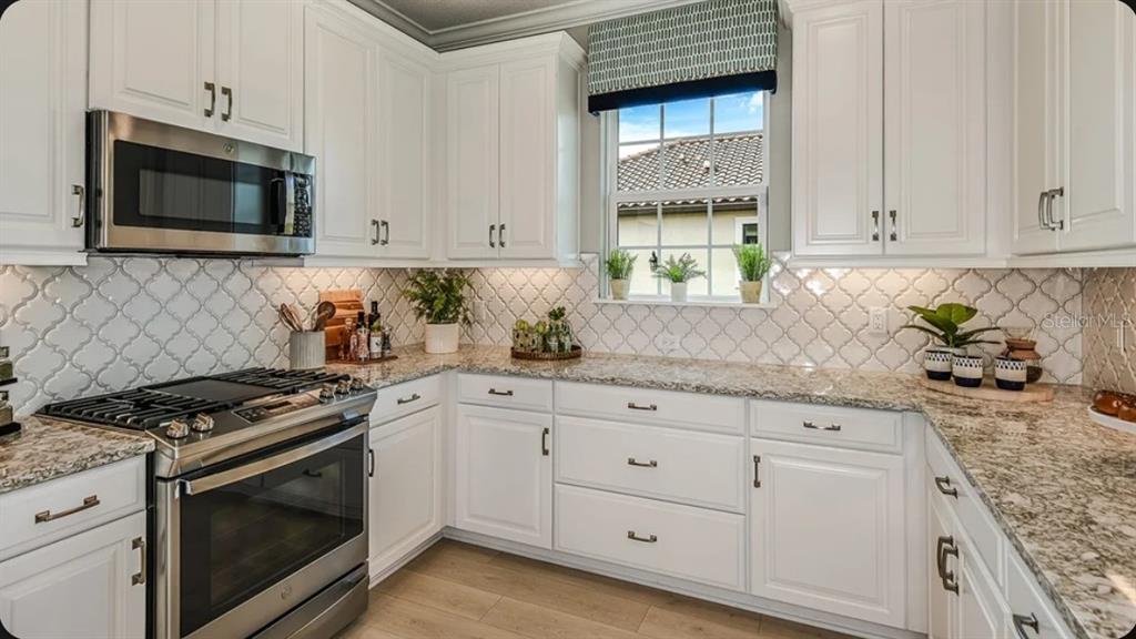A kitchen with white cabinets, stainless steel appliances, granite countertops, and a patterned tile backsplash — 14513 DERNA TERRACE, BRADENTON, FL