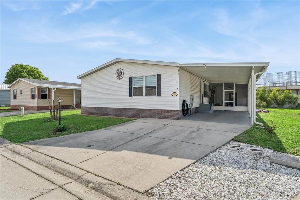 A single-story manufactured home with white siding, a brick base, and an attached carport — 2463 INDEPENDENCE LANE, ST CLOUD, FL