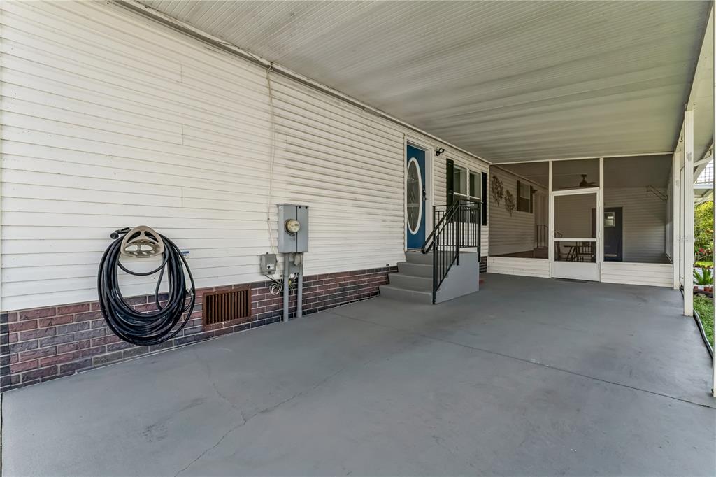 A concrete carport leads to a blue front door with stairs and a screened porch — 2463 INDEPENDENCE LANE, ST CLOUD, FL