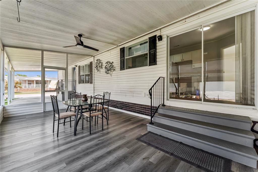 A covered patio features wood-look flooring, a dining set, and stairs leading to a sliding door — 2463 INDEPENDENCE LANE, ST CLOUD, FL
