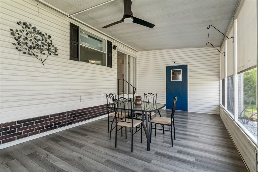 A covered patio features gray wood-look flooring, a dining set, and a blue exterior door — 2463 INDEPENDENCE LANE, ST CLOUD, FL