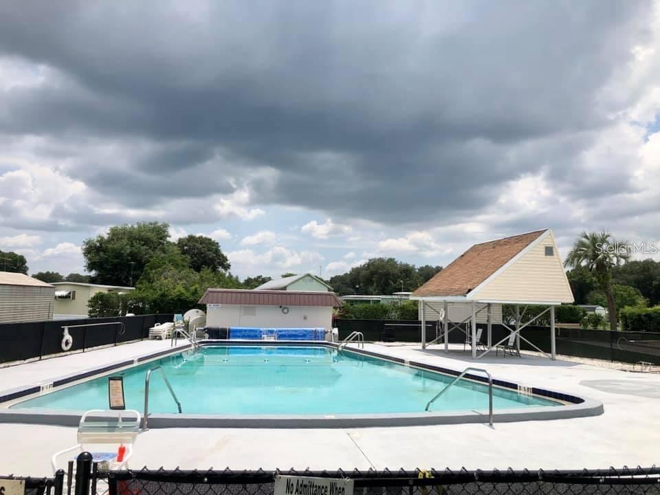 An outdoor swimming pool with a covered seating area and a small utility building — MONET DRIVE, ZEPHYRHILLS, FL