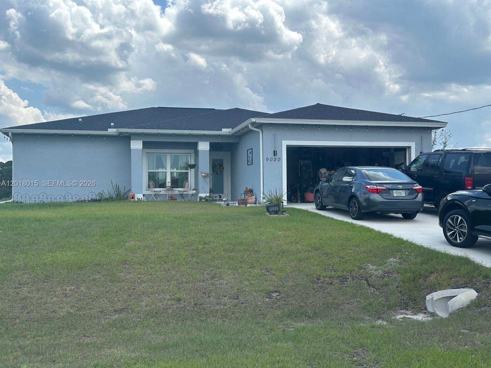 A single-story blue house with a two-car garage and a front lawn under cloudy skies — 9020 W MAC CT, La Belle FL 33935, LA BELLE, FL