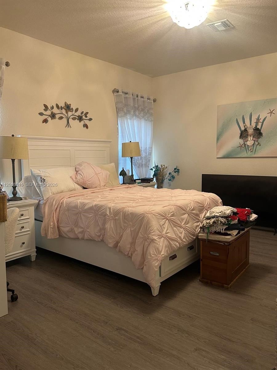 A bedroom features a white bed with pink bedding, wood-look flooring, and a wall-mounted television — 9020 W MAC CT, La Belle FL 33935, LA BELLE, FL