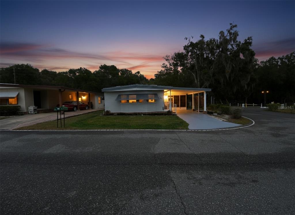 A single-story manufactured home with a carport and lawn at sunset — 164 ROYAL PALM DRIVE, LEESBURG, FL