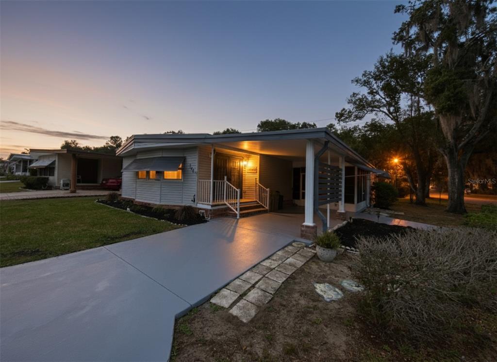 A single-story house with a gray exterior, a carport, and a paved driveway at dusk — 164 ROYAL PALM DRIVE, LEESBURG, FL