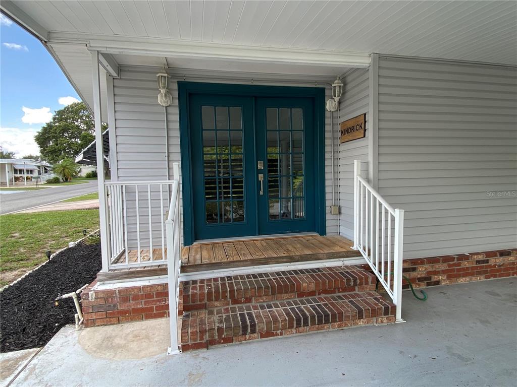 A set of teal double doors with glass panes sits atop brick steps under a carport — 164 ROYAL PALM DRIVE, LEESBURG, FL