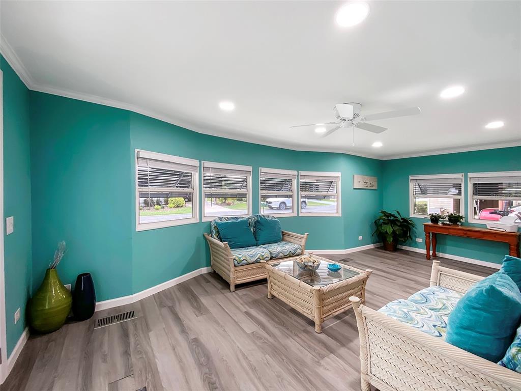 A living room with teal walls, light wood-look flooring, wicker furniture, and multiple windows — 164 ROYAL PALM DRIVE, LEESBURG, FL