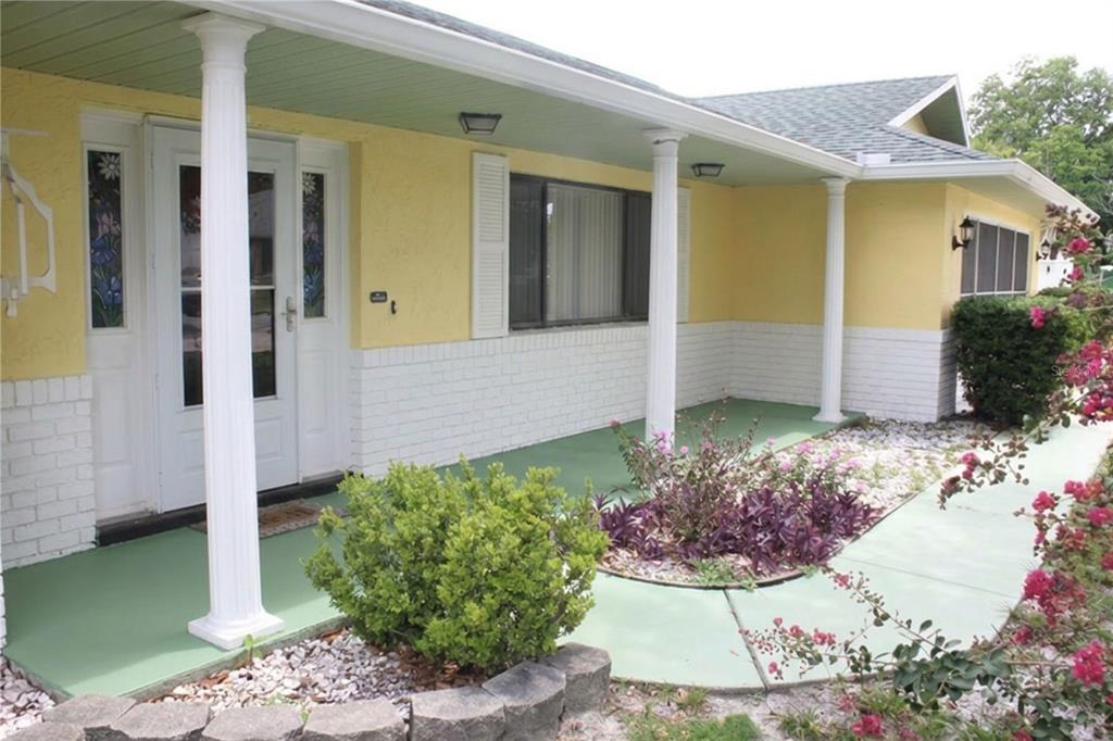 A yellow house exterior features a white brick base, green porch flooring, and white columns — 2203 INDIA BLVD, DELTONA, FL