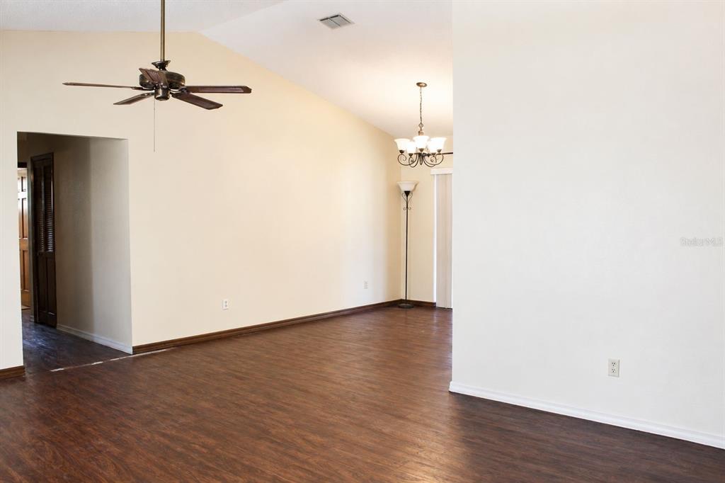 An empty room with wood-look flooring, a vaulted ceiling, a ceiling fan, and a chandelier — 2203 INDIA BLVD, DELTONA, FL