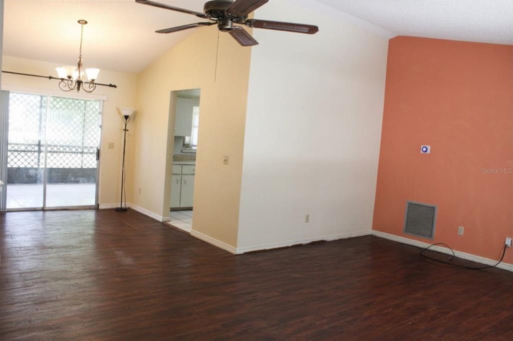 A living room with dark wood-look flooring, a ceiling fan, and an orange accent wall — 2203 INDIA BLVD, DELTONA, FL
