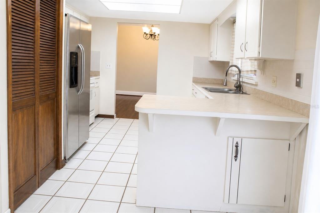 A kitchen features white cabinets, a laminate countertop, a stainless steel refrigerator, and tiled flooring — 2203 INDIA BLVD, DELTONA, FL