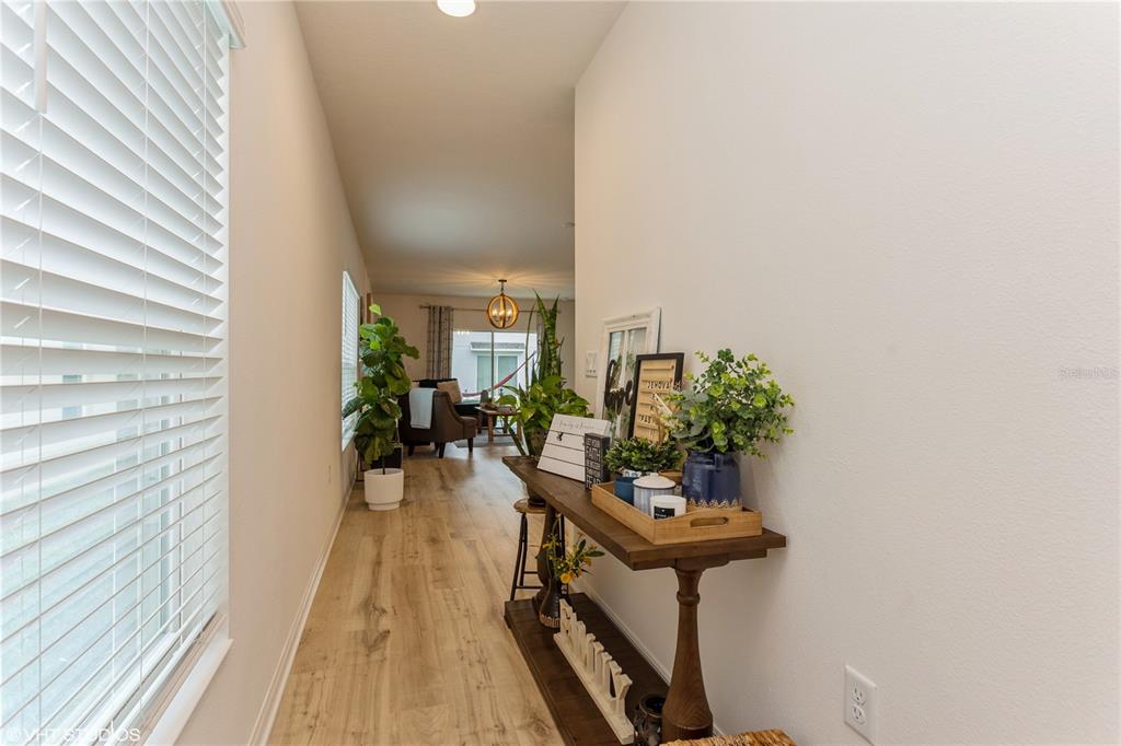 A hallway with light wood-look flooring leads toward a living area with a pendant light — 6985 WILSON PASTURE AVENUE, GROVELAND, FL
