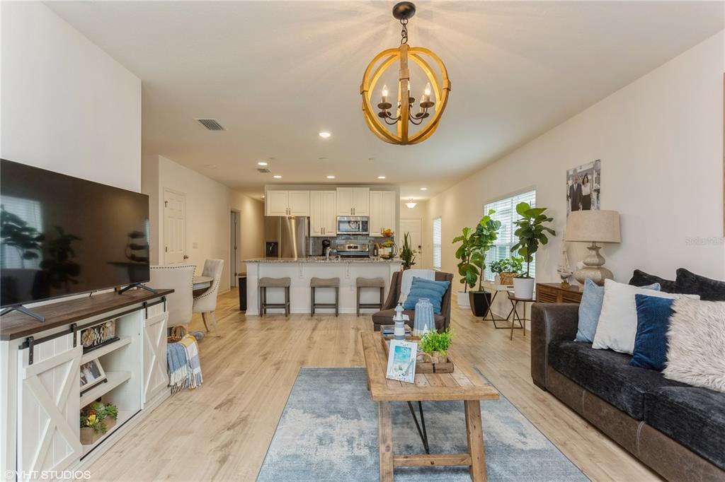 An open-concept living room features light wood flooring, a kitchen island, and a wooden chandelier — 6985 WILSON PASTURE AVENUE, GROVELAND, FL