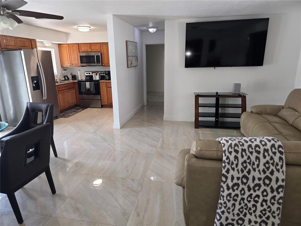 A living room with tile floors and a wall-mounted television opens to a kitchen — 537 MELODY CIRCLE, SARASOTA, FL