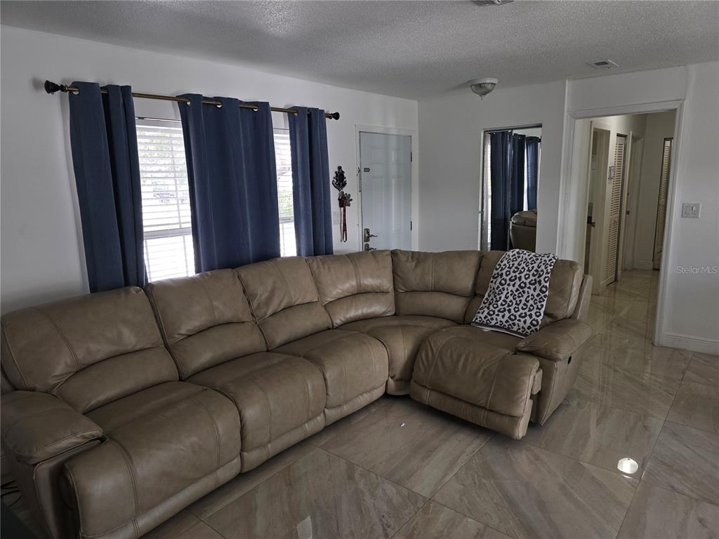 A living room features a large tan sectional sofa, blue curtains, and light-colored tile flooring — 537 MELODY CIRCLE, SARASOTA, FL