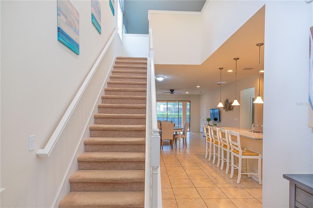 A carpeted staircase leads to an upper level beside an open kitchen and dining area — 1888 GOBI DRIVE, KISSIMMEE, FL