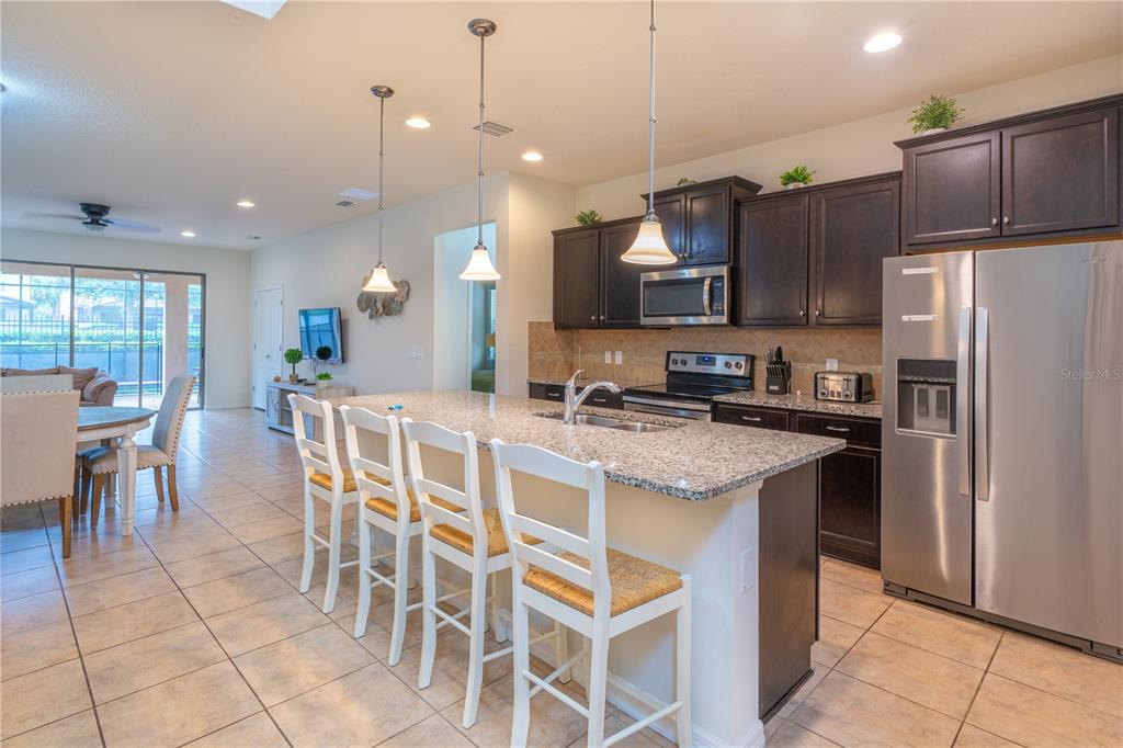 A kitchen features dark wood cabinets, granite countertops, a center island with bar seating, and stainless-steel appliances — 1888 GOBI DRIVE, KISSIMMEE, FL