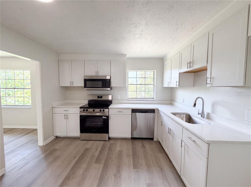 A kitchen features white cabinets, stainless steel appliances, and light wood-look flooring — 333 E CHELSEA STREET, DELAND, FL