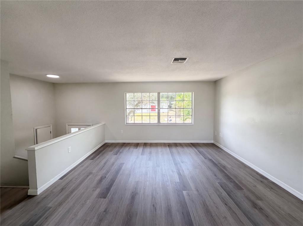 An empty room with light gray walls, wood-look flooring, and a large window — 333 E CHELSEA STREET, DELAND, FL